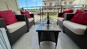 A balcony with wicker furniture, a glass table, and a bottle of wine. - Spacious, family-friendly apartment, 5 min from La Mata Beach (La Mata)