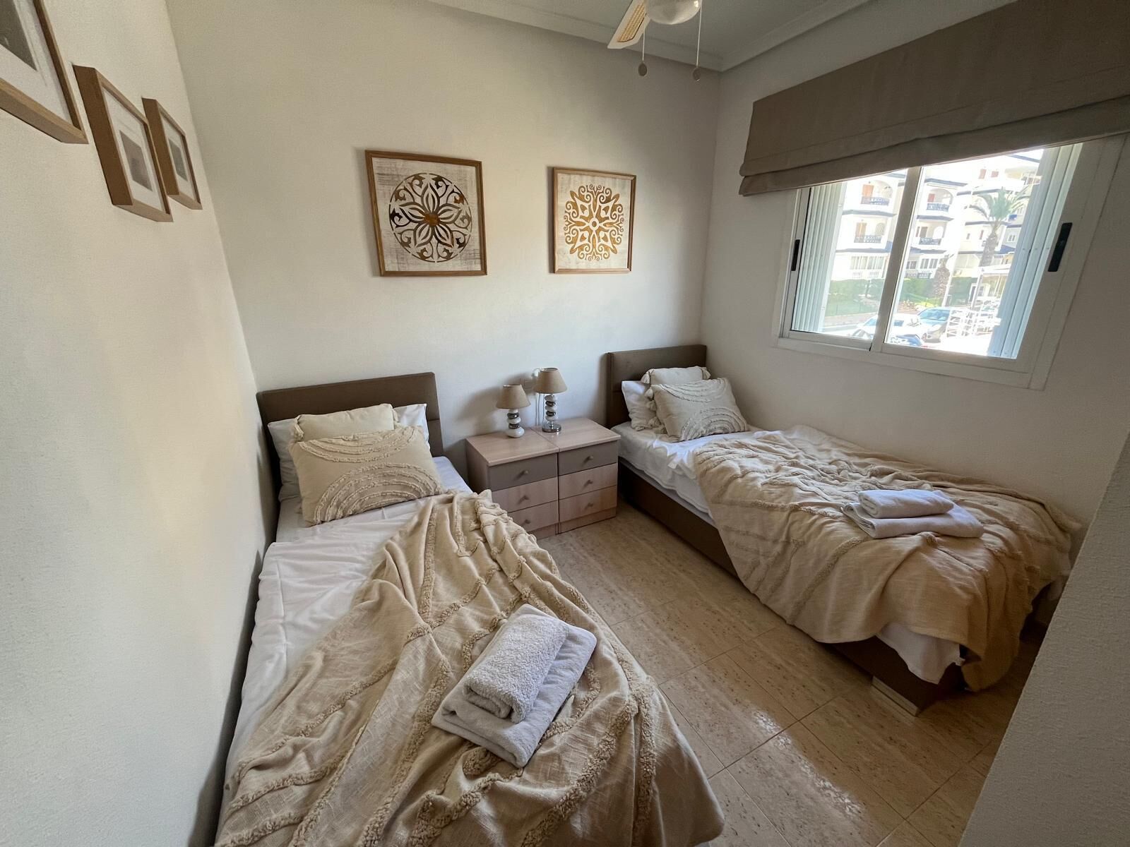 Une chambre avec deux lits, une table de chevet et une fenêtre donnant sur des immeubles.