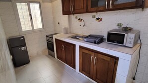A compact kitchen with white marble tiles, a refrigerator, a stove, and a microwave. - OUAKAM self-contained studio 10m from the monument (Ouakam)