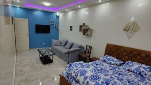 A modern bedroom with a bed, a sofa, a TV, and a wall-mounted shelf. - OUAKAM self-contained studio 10m from the monument (Ouakam)