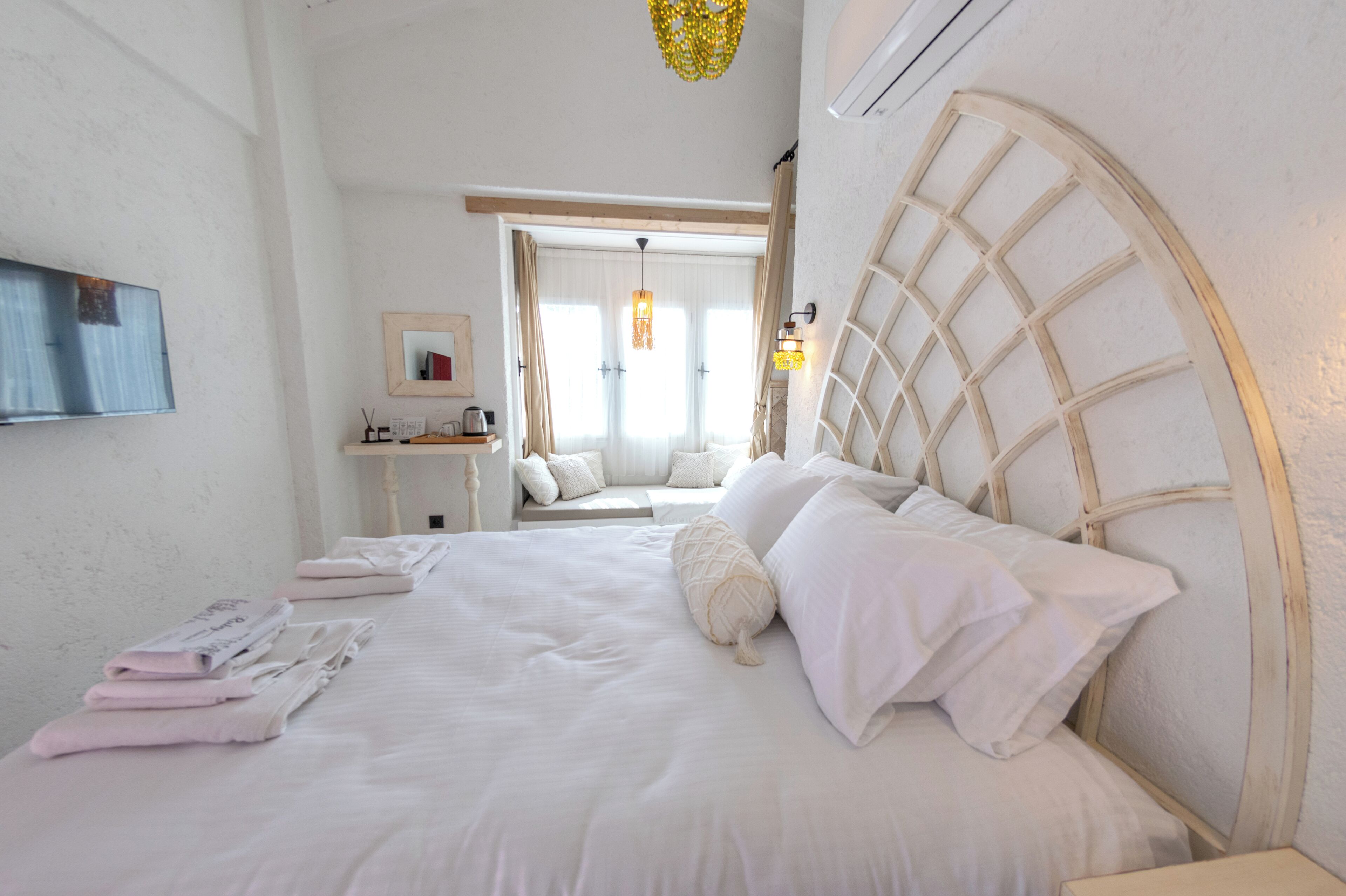 Un lit bien fait, avec du linge de lit blanc et des oreillers, une table de chevet avec une lampe et une fenêtre avec des rideaux.