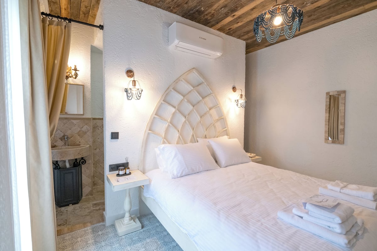 Une chambre à coucher avec un grand lit, une table de chevet, une commode, un climatiseur fixé au mur et un luminaire décoratif.
