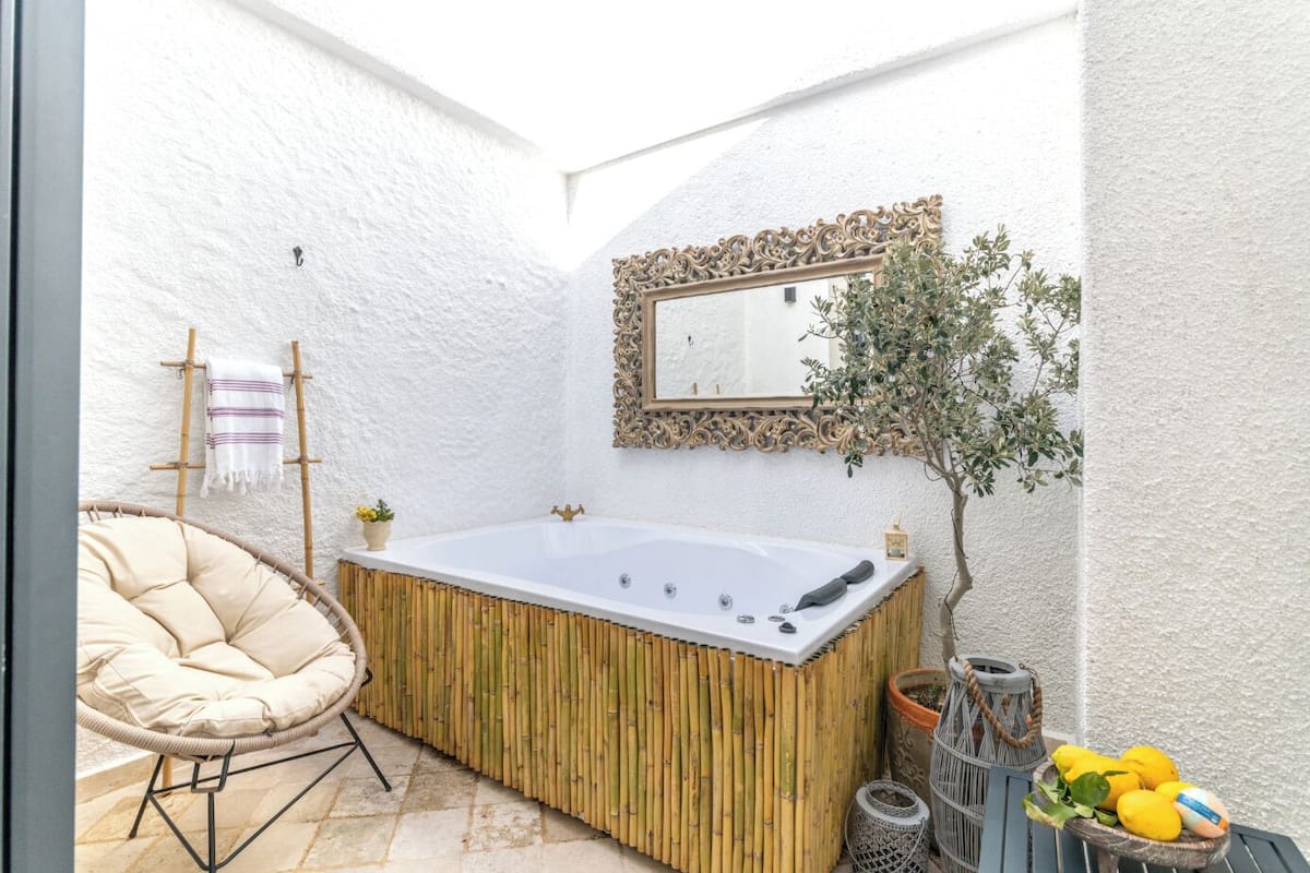 Un espace détente avec un jacuzzi, un fauteuil en osier, une petite plante en pot et un miroir au mur.