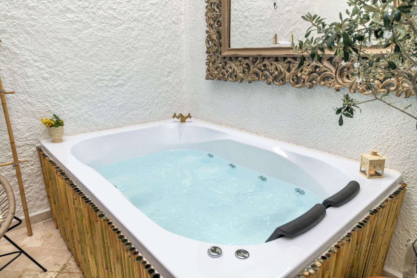 Un jacuzzi con estructura de madera, una planta pequeña y un espejo decorativo en la pared.