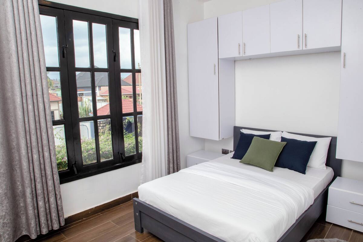 A bedroom with a bed, white wardrobe, and a window with curtains.
