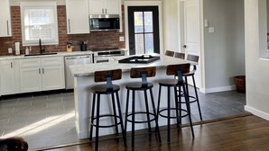 A modern kitchen with white cabinets, a built-in microwave, and a central island with bar stools.