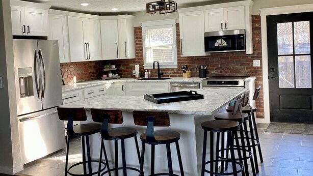 A modern kitchen with white cabinets, a central island with bar stools, a stainless steel refrigerator, and a microwave.