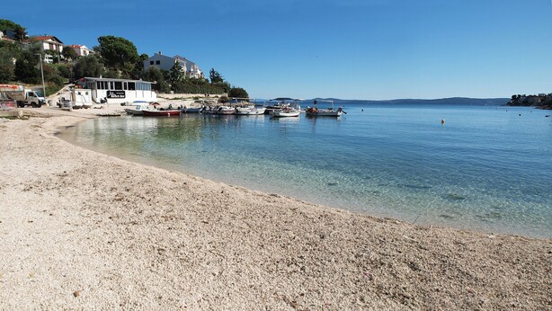 Une plage où sont amarrés des bateaux, un bâtiment abritant un bar, et des maisons en arrière-plan.