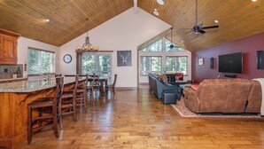A spacious living area with a high ceiling, wooden flooring, a dining area with a large table and chairs, a seating area with couches, and a television mounted on the wall.