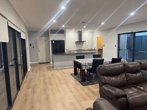 A modern kitchen with a central island, a dining area with a table and chairs, and a leather sofa. - The Dreamy Retreat in Averley (Aveley)