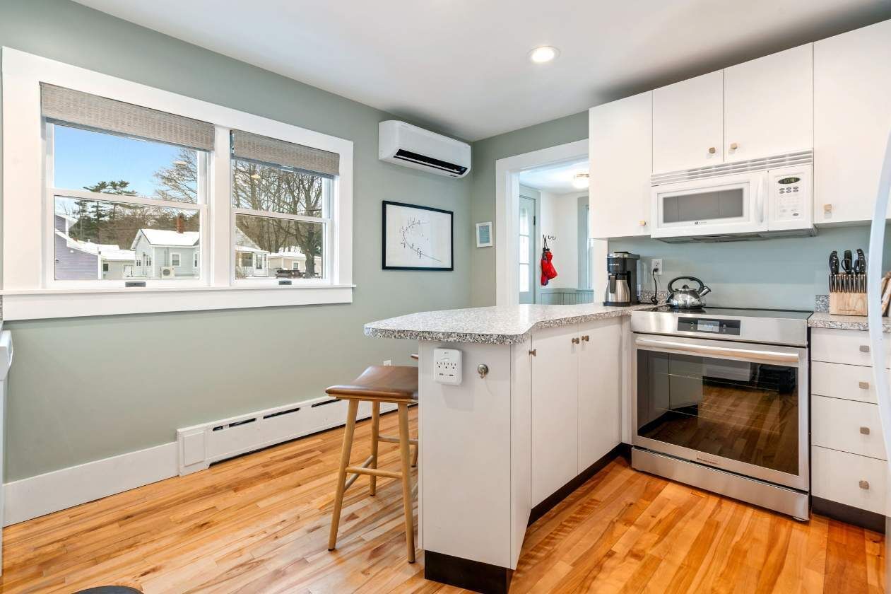 A modern kitchen with a central island, white cabinets, a stainless steel oven, and a microwave.