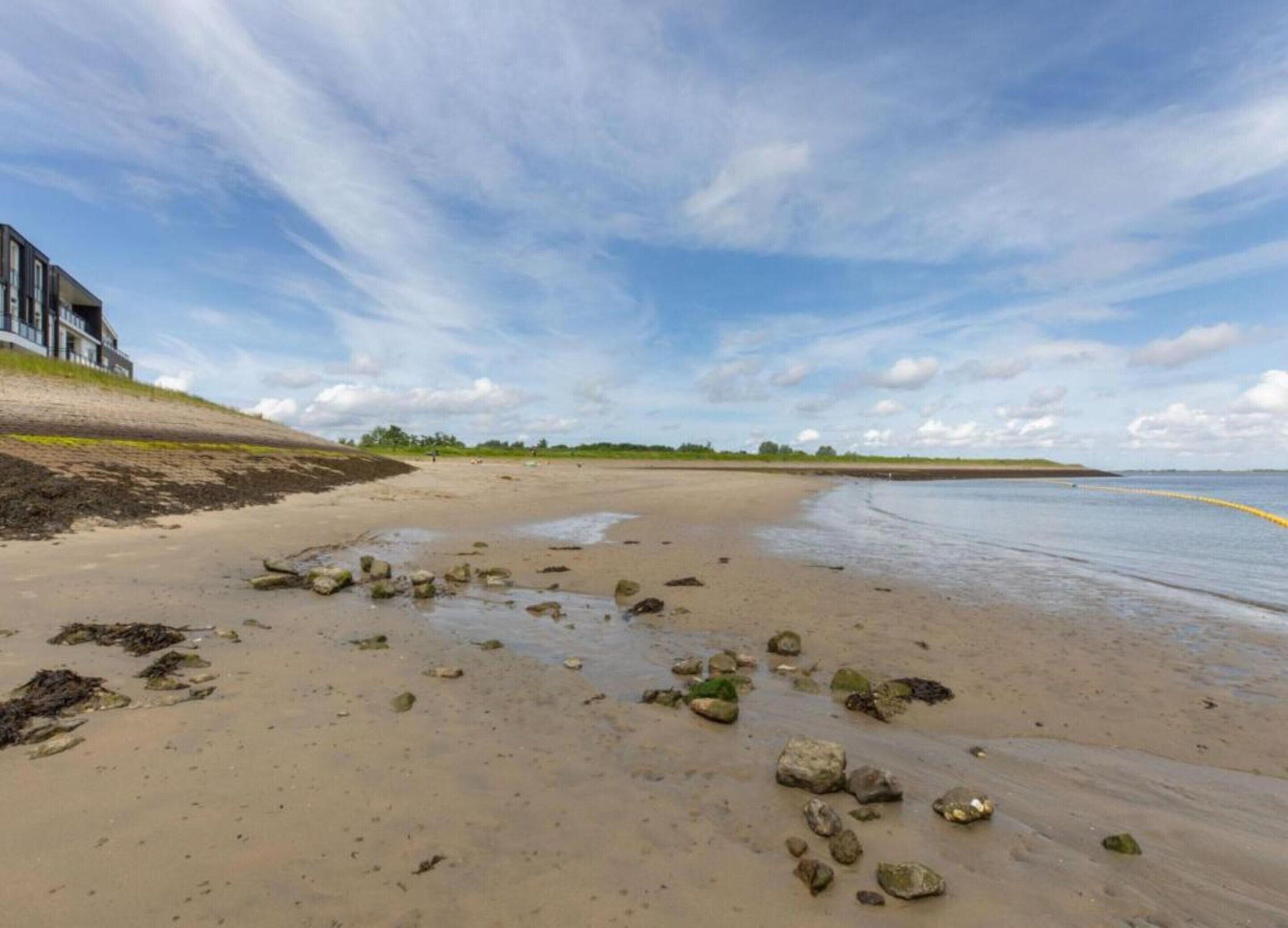 Ein sandiger Strand mit vereinzelten Felsen und einem klaren Himmel.