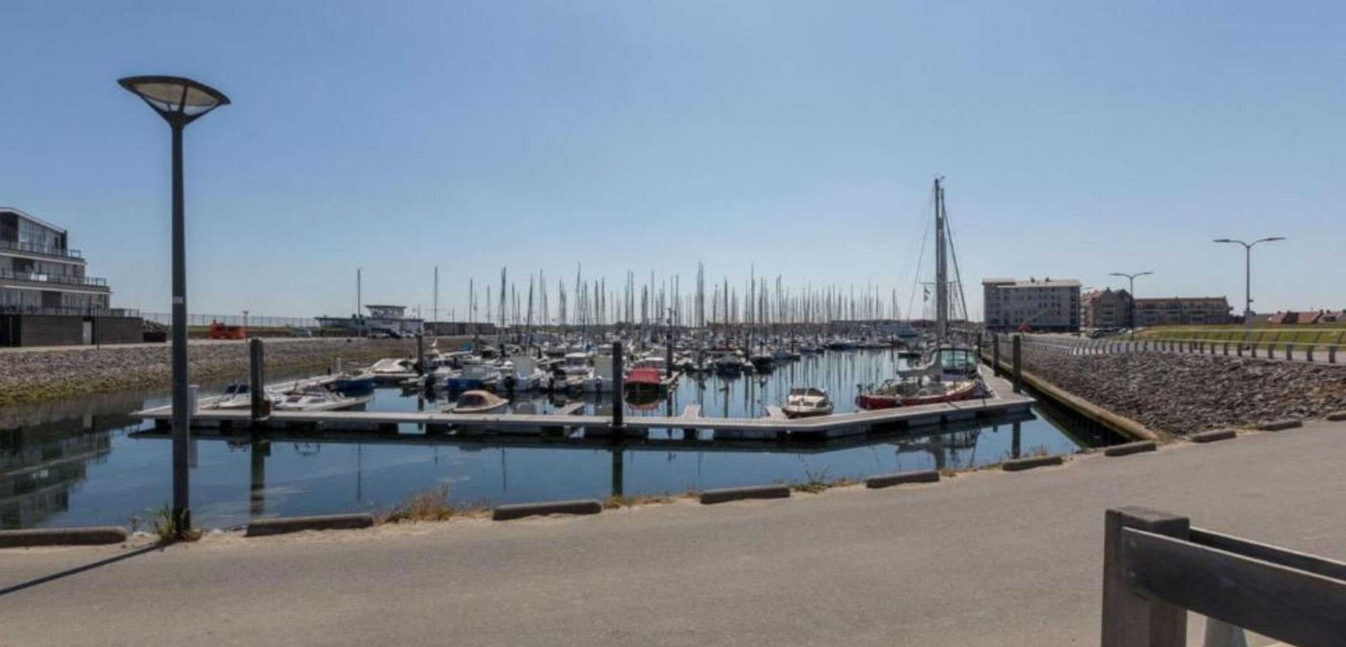 A marina with multiple boats docked, a lamp post, and a building in the background.