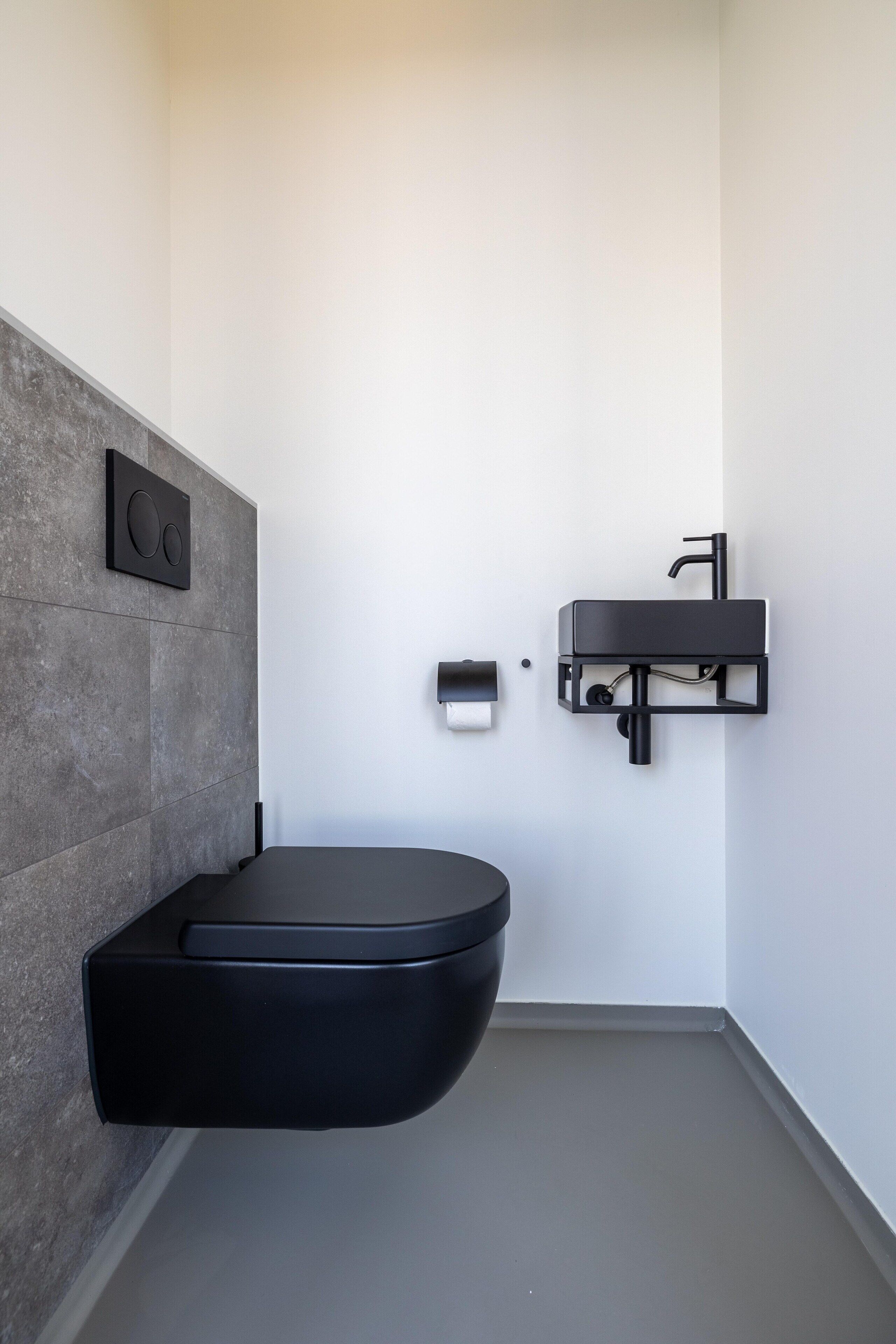 A modern bathroom with a built-in toilet, a wall-mounted sink, and a towel dispenser.