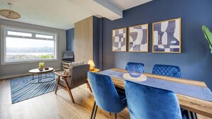 A modern dining area with a wooden table, blue upholstered chairs, and abstract wall art.