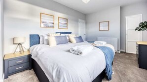A modern bedroom with a large bed, bedside tables, a lamp, and framed artwork on the walls.