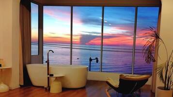A modern bathroom with a large window, a bathtub, a chair, and a potted plant.