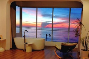 A modern bathroom with a large window, a bathtub, a chair, and a potted plant.