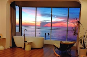 Un baño moderno con un ventanal grande, una bañera, una silla y una planta en maceta.
