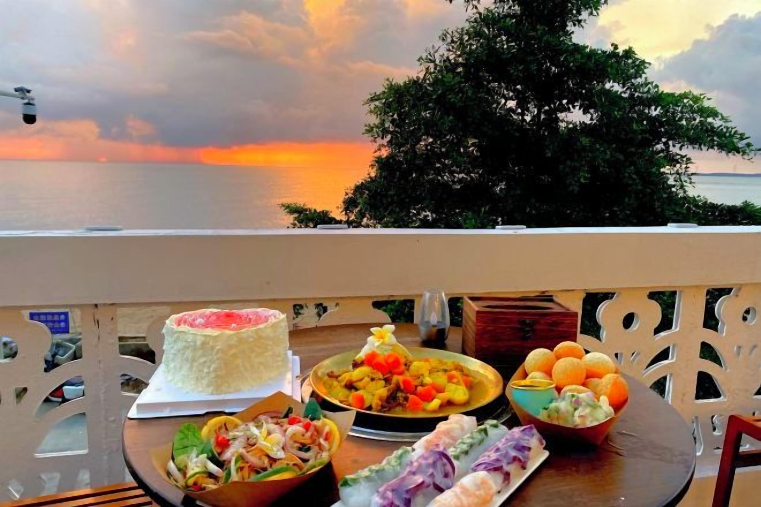 A table with food items and a cake on a balcony overlooking the sea.