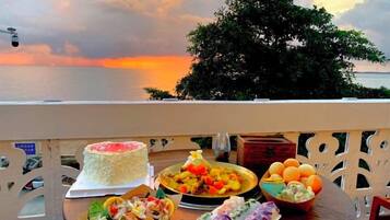 A table with food items and a cake on a balcony overlooking the sea.