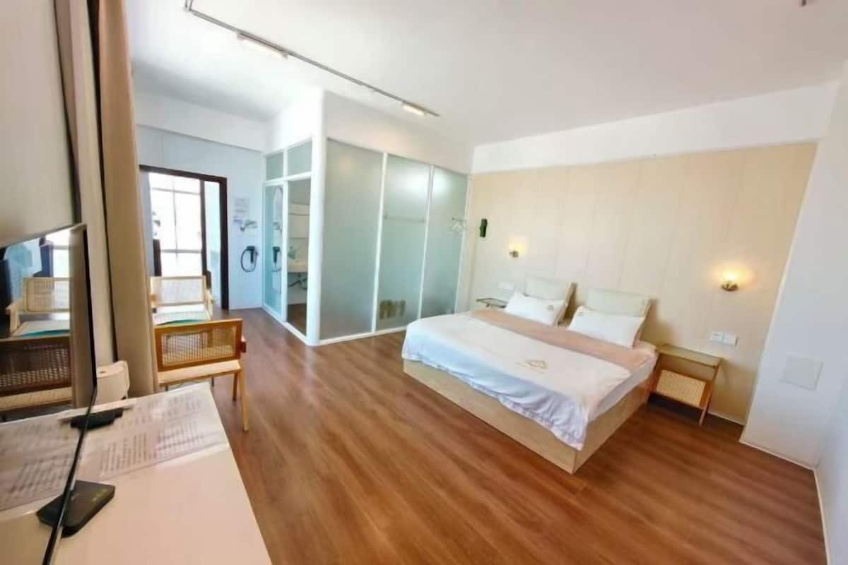 Ein modernes Hotelzimmer mit Holzboden, einem Bett mit weißer Bettwäsche, einem Schreibtisch mit Stuhl und einem großen Fenster.