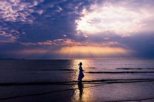 Una persona está de pie en una playa con un atardecer de fondo.