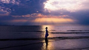 A person standing on a beach at sunset with the ocean in the background.