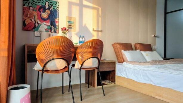 A bedroom with a bed, two wicker chairs, a desk, and a painting on the wall.