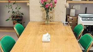 A wooden dining table with four green chairs, a vase with pink flowers, and a white object on the table.