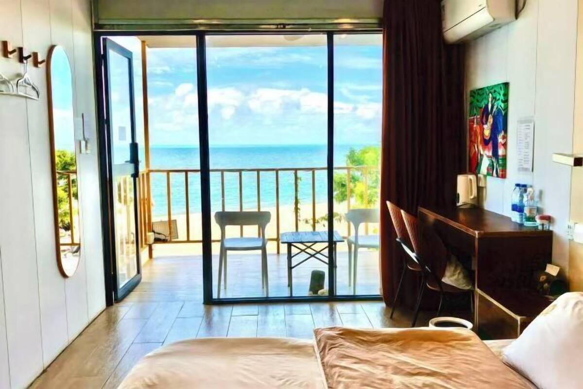 Ein Hotelzimmer mit Bett, Schreibtisch, Stuhl, kleinem Tisch und Blick auf den Strand durch eine Schiebetür.
