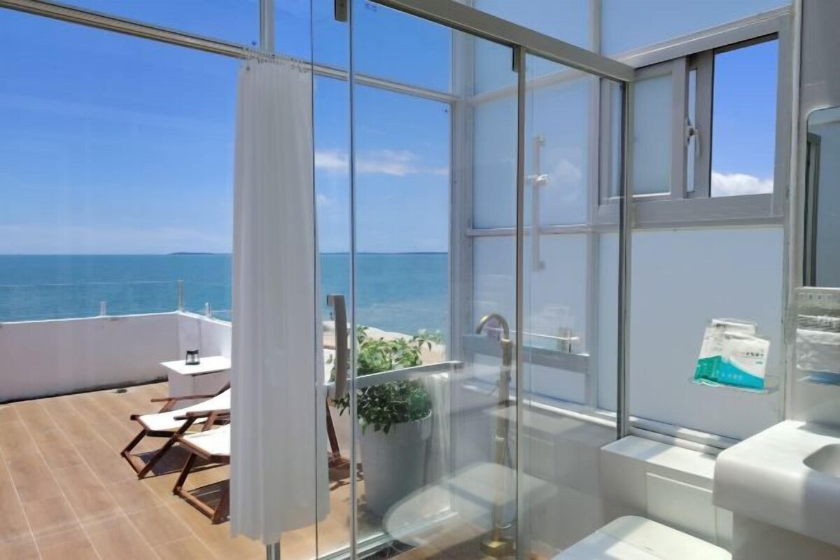 A balcony with a view of the sea, a glass shower enclosure, and a white sink.