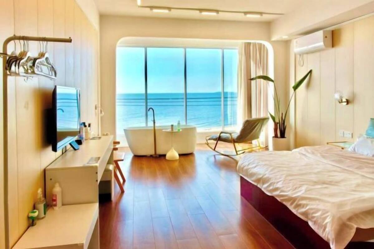 Ein modernes Hotelzimmer mit großem Fenster, einer Badewanne, einem Bett und einem Fernseher.