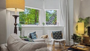 A cozy living room with a sofa, a small table, a lamp, and a view of a balcony.