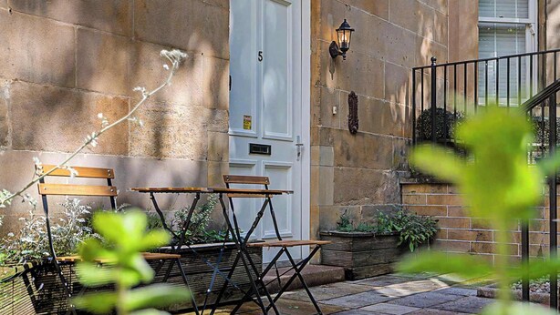 A stone building with a white door, outdoor seating, and a small garden area.