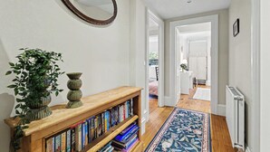 A hallway with a wooden bookshelf, a mirror, and a patterned rug.