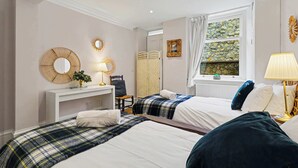 A hotel room with two beds, a desk, a chair, a mirror, a window with a view of rocks, and a lamp.