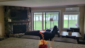 A living room with a stone fireplace, a large window with a view of a grassy area, and a dining area with a table and chairs. - Relax and Recharge: Mille Lacs Lake Beach Villa - Completely Remodeled (Onamia)
