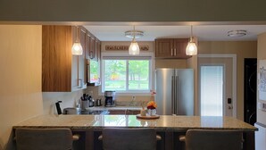 A modern kitchen with wooden cabinets, a stainless steel refrigerator, and a large island with bar stools. - Relax and Recharge: Mille Lacs Lake Beach Villa - Completely Remodeled (Onamia)