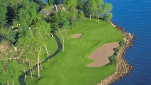 An aerial view of a golf course with a water body on one side and a forested area on the other. - Relax and Recharge: Mille Lacs Lake Beach Villa - Completely Remodeled (Onamia)