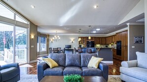 Amplia sala de estar con un sofá seccional gris oscuro, una mesa de centro con una planta y vistas al área de cocina y comedor.