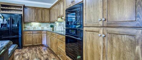Eine Küche mit Holzschränken, einem schwarzen Kühlschrank und einem eingebauten Backofen.