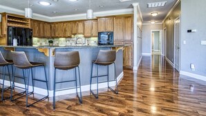 Una cocina moderna con armarios de madera, una isla central con taburetes de bar y un refrigerador de acero inoxidable.