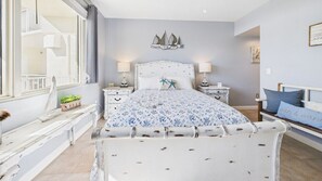 Une chambre avec un grand lit, deux tables de chevet, une fenêtre donnant sur un balcon et un élément décoratif mural au-dessus du lit.
