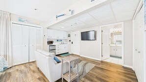 Een compacte hotelkamer met kitchenette, een zithoek met een bank en salontafel, een aan de muur bevestigde televisie en een badkamer met douche en toilet.