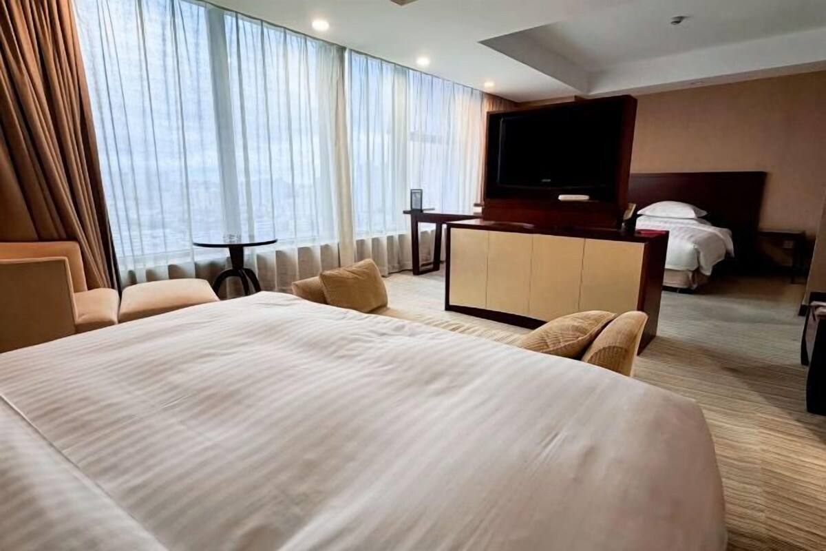 A hotel room with a large bed, a desk, a television, and a view of the city.