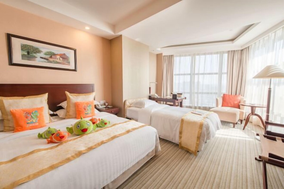 A hotel room with two beds, a desk, a chair, and a large window.