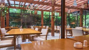An indoor dining area with wooden tables and chairs, large windows, and a wooden ceiling structure.