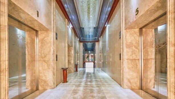 Un pasillo con pisos y paredes de mármol, puertas numeradas y un candelabro.