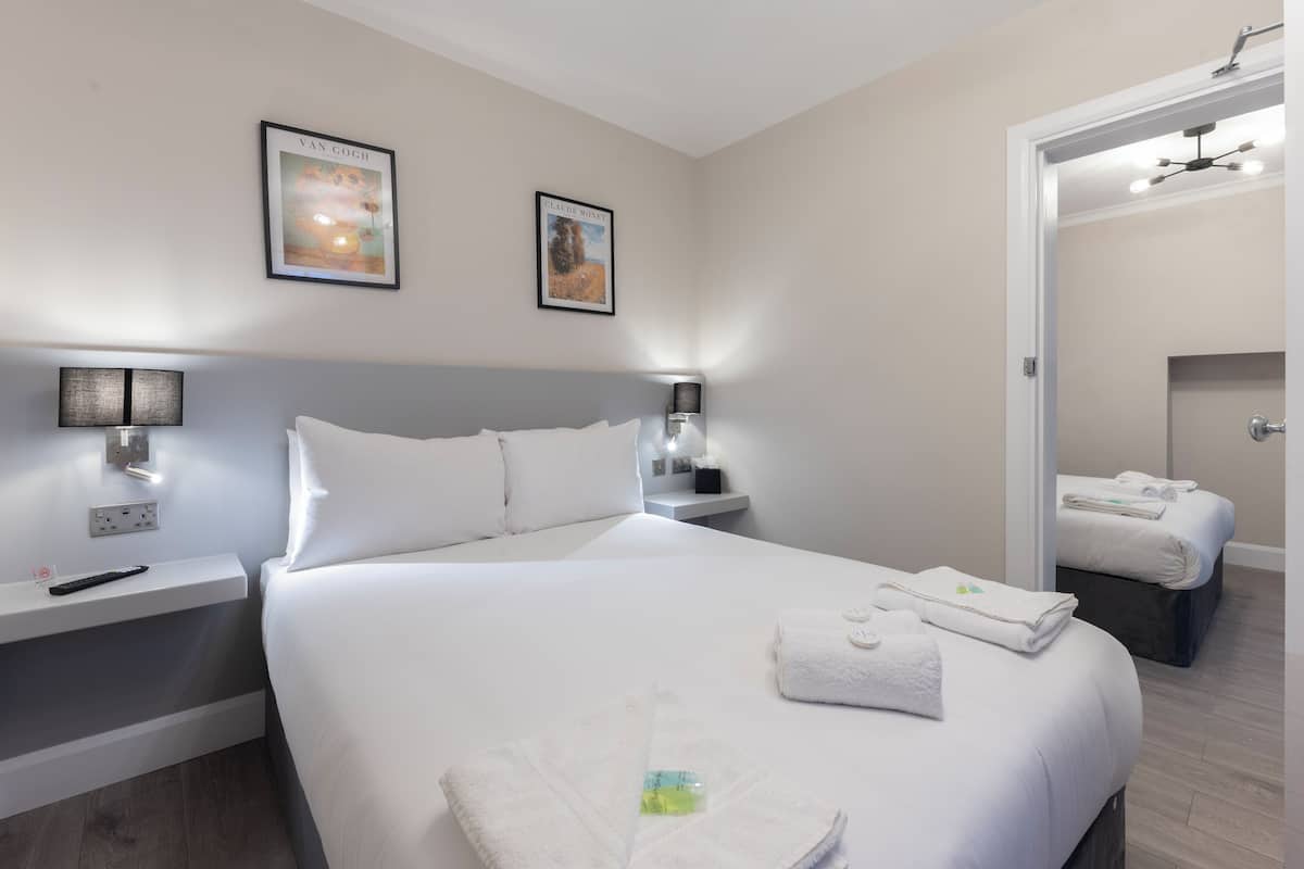 A hotel room with a large bed, two bedside tables with lamps, a wall-mounted TV, and framed artwork.